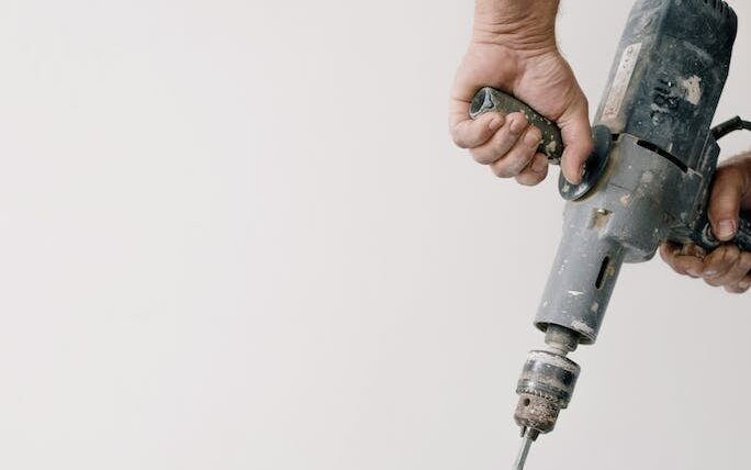 Crop unrecognizable male worker holding drill with tool and mixing cement in plastic container